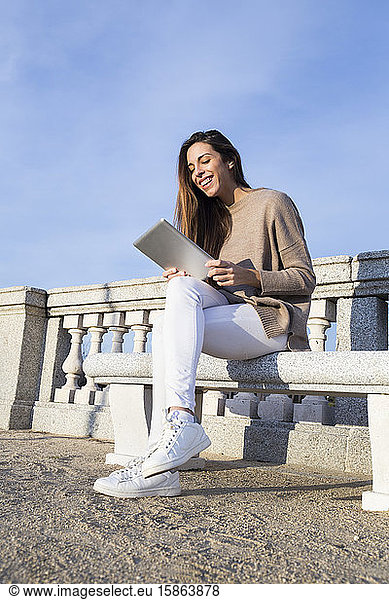 Laughing woman using her tablet while seated on a bench
