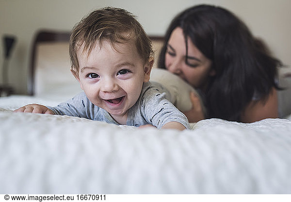 Laughing year old baby on stomach on bed with playful mid-30's mother