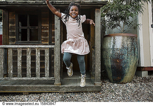 Laughing young black girl with long braids jumping from cabin porch