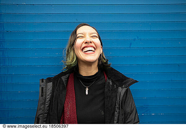 Laughing young woman with closed eyes on blue wall  in rain.