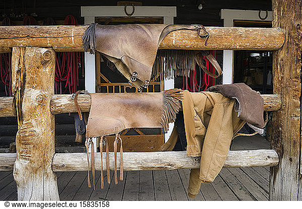 Leather chaps hang on a wood porch railing after horseback riding