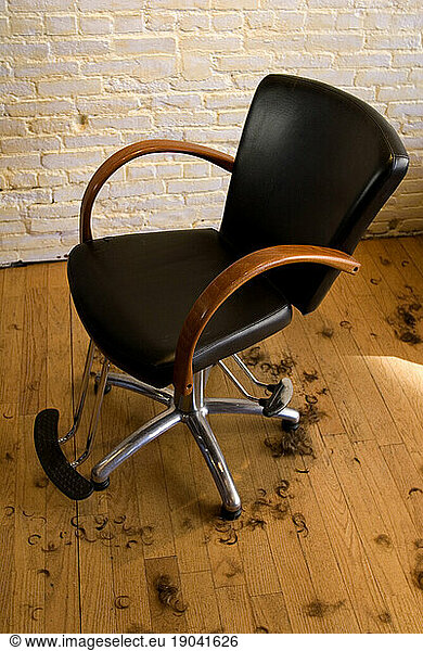 Leather salon chair with hair clippings on wood floor.