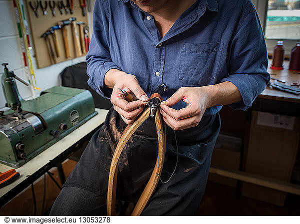 Leatherworker stitching leather in workshop  mid section