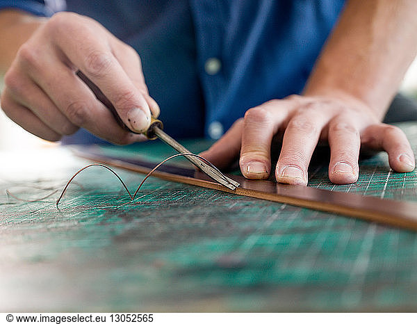 Leatherworker trimming leather for handbag strap in workshop  close up of hands