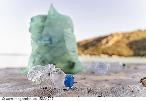 Leere Plastikflaschen und Mülleimer voller gesammelter Plastikflaschen am Strand