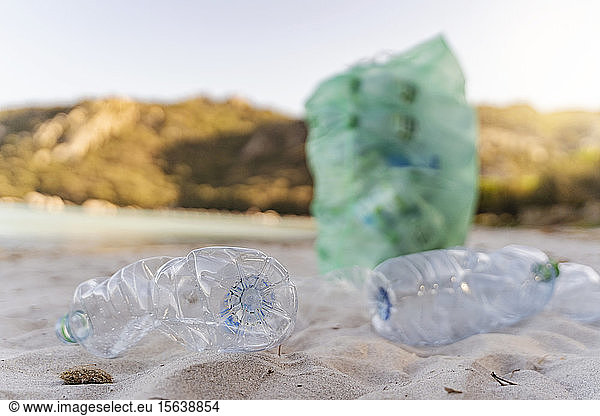 Leere Plastikflaschen und Mülleimer voller gesammelter Plastikflaschen am Strand