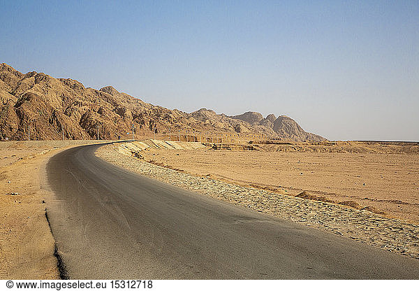 Leere Straße durch eine Felsformation in der Wüste bei strahlend blauem Himmel