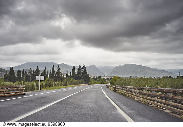 Leere Straße durch ländliche Landschaft  graue Wolken oben  Mallorca  Spanien