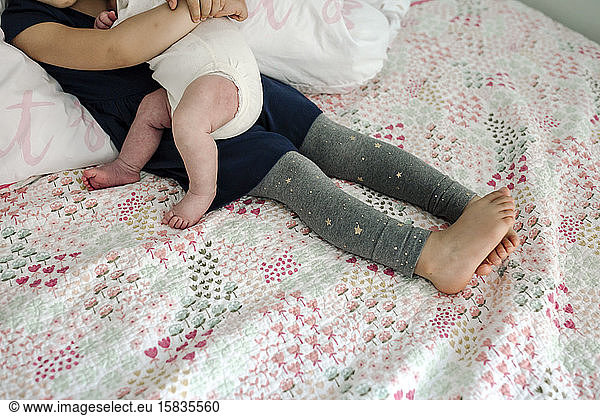 Legs and bare feet of young girl on bed cuddling newborn baby