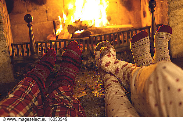 Legs and feet of three people wearing pyjamas and warm socks lying in front of a fireplace.