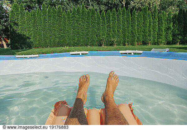Legs of man floating in wading swimming pool at backyard