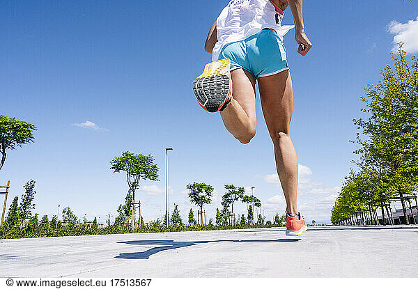 Legs of mid adult woman running on road against blue sky during sunny day