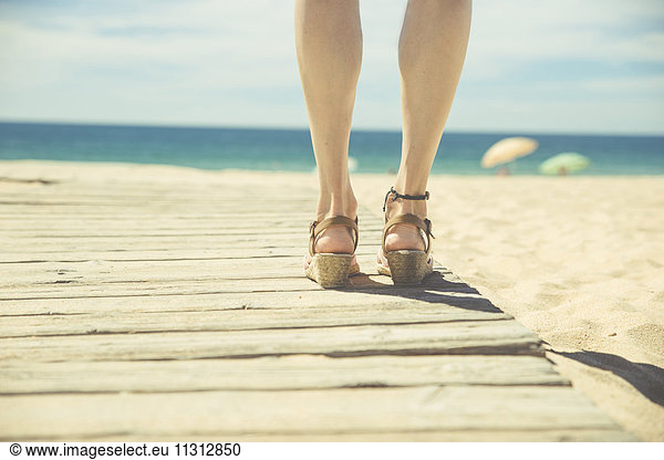 Legs of woman standing at boardwalk on the beach