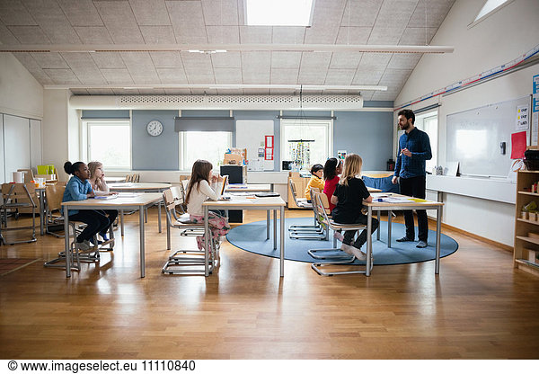 Lehrer  der die Schüler in einem hell erleuchteten Klassenzimmer unterrichtet.