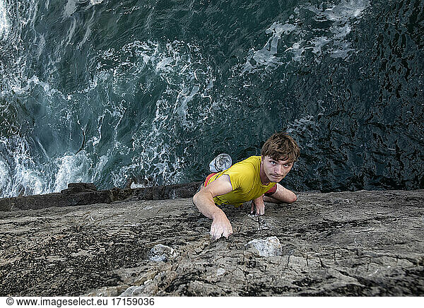 Leidenschaftlicher junger männlicher Kletterer klettert auf Felsen am Meer