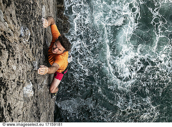 Leidenschaftlicher männlicher Felskletterer klettert an einer Felswand am Meer