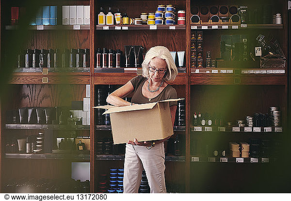 Leitende Verkäuferin beim Auspacken von Karton gegen Regal im Feinkostladen