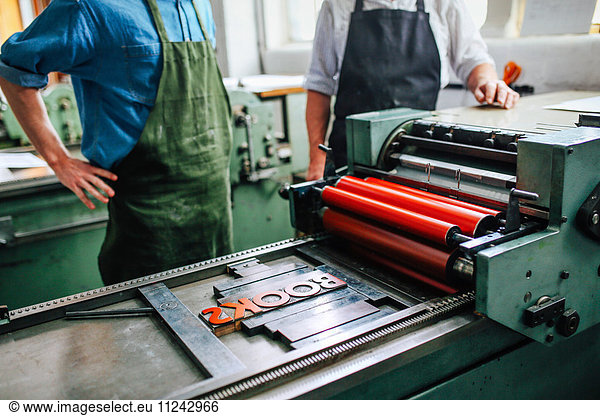 Leitender Handwerker/Techniker unter Aufsicht eines jungen Mannes an einer Buchdruckmaschine in der Buchkunstwerkstatt  mittlerer Abschnitt