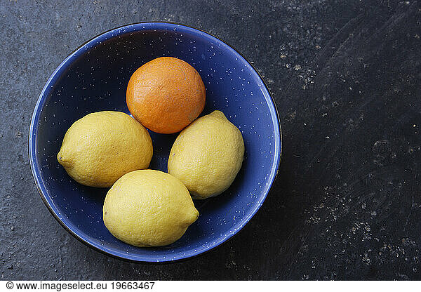 Lemons and an orange in a blue bowl.
