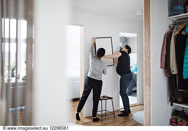 Lesbian couple arranging paintings on wall at home