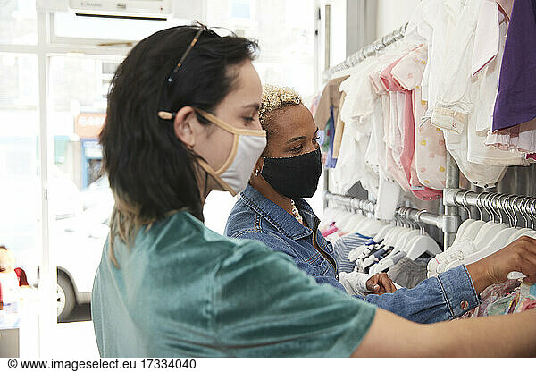 Lesbian couple choosing kid's clothes in store during pandemic