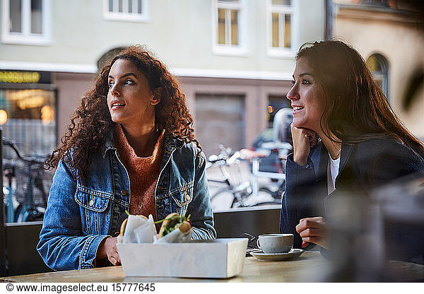 Lesbian couple looking while sitting at sidewalk cafe during weekend in city