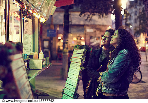 Lesbian couple standing against concession stand in city at night