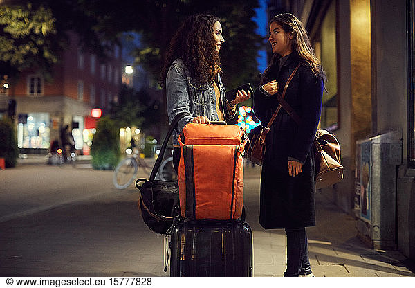 Lesbian couple with luggage standing on sidewalk in city at night