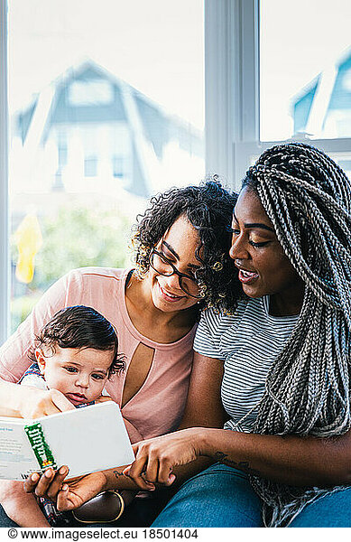 Lesbian mothers showing picture book to cute son at home