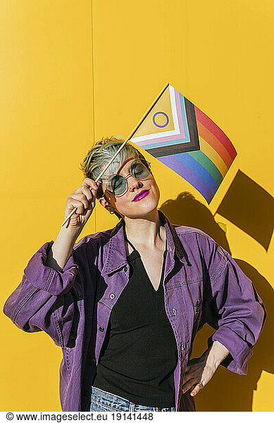 Lesbian woman holding multi colored flag in front of yellow wall