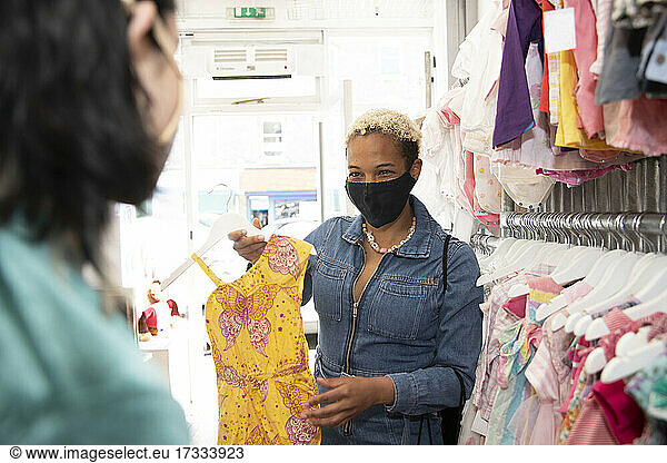Lesbian woman wearing protective face mask showing dress to girlfriend at store