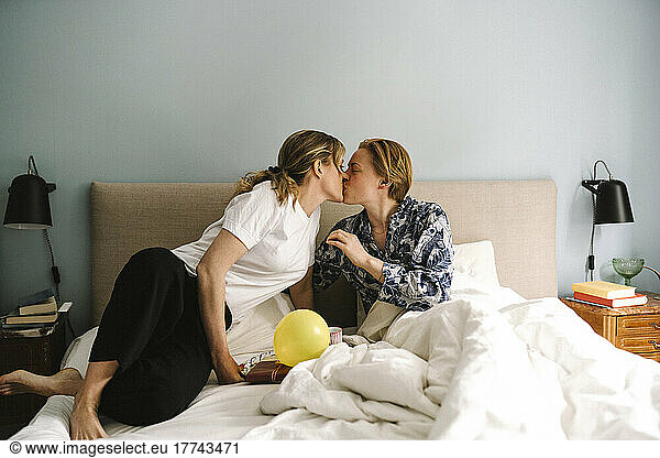 Lesbian woman with birthday present kissing girlfriend on bed at home