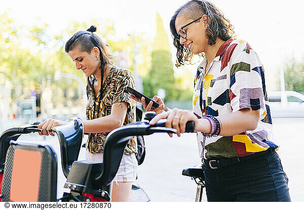 Lesbisches Paar benutzt Smartphone  um Elektrofahrrad in der Stadt zu entriegeln