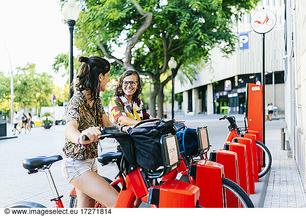 Lesbisches Paar lächelt sich gegenseitig an  während es an einer Fahrradabstellanlage steht