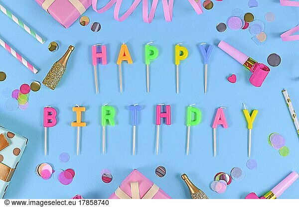 Letter canles forming text Happy Birthday with confetti and paper streamers on blue background