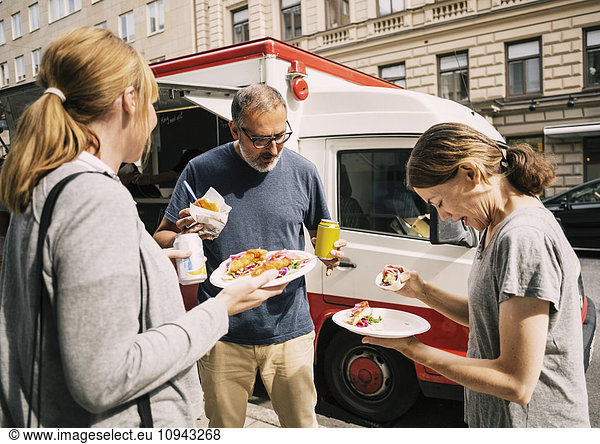 Leute  die Essen essen  während sie auf der Straße stehen.