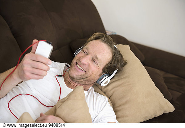 liegend liegen liegt liegendes liegender liegende daliegen Mann Kopfhörer Couch Smartphone