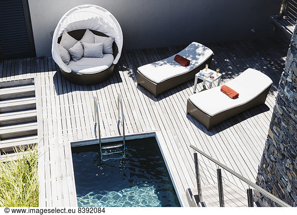 Liegestühle auf Holzterrasse am modernen Pool