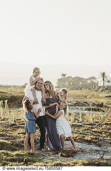 Lifestyle portrait of family with young girls smiling at beach sunset
