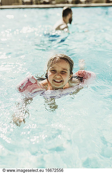 Lifestyle portrait of young girl swimming in hotel pool on vacation