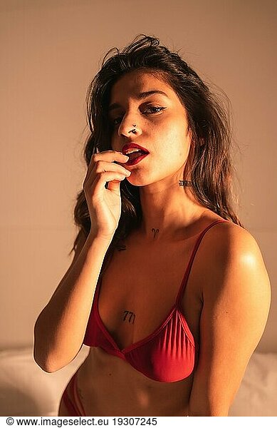 Lifestyle  sexy brunette Caucasian girl with a red tight corset  sensual perched on the bed  illuminated with dim light at night in the room