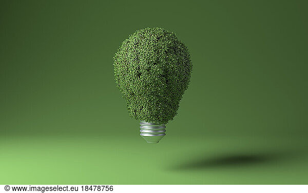 Light bulb covered with green plants against colored background