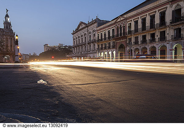 Light trails on city street by buildings at dusk
