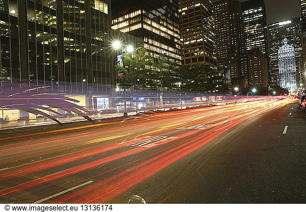 Light trails on city street by illuminated buildings