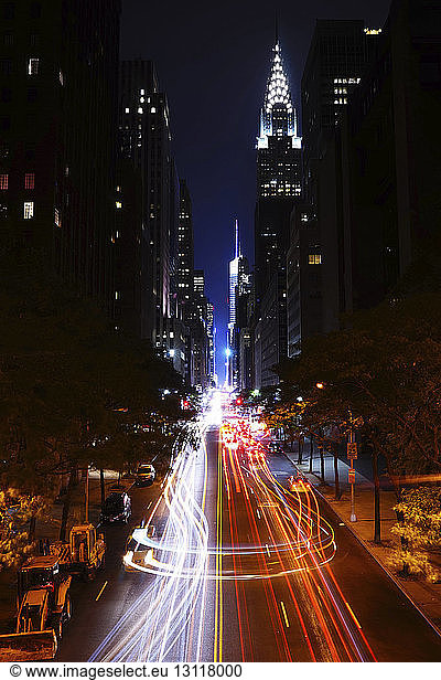 Light trails on city street by illuminated buildings at night