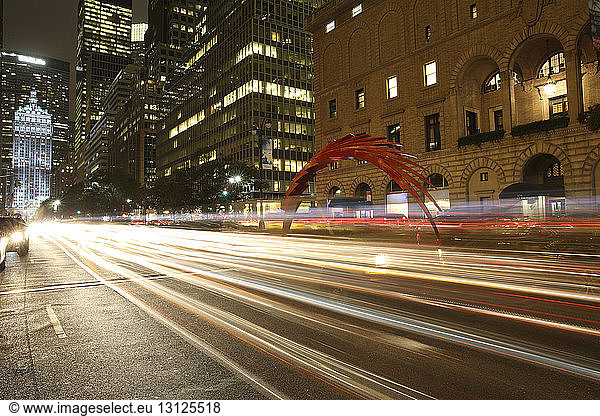 Light trails on road by illuminated buildings