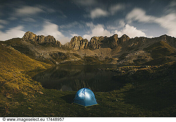 Lighted tent against rugged mountains and lake  Pyrenees.