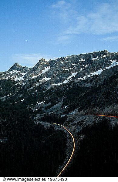 Lights from a car line the road as the final light sets on the soaring peaks of North Cascades National Park  WA  USA.