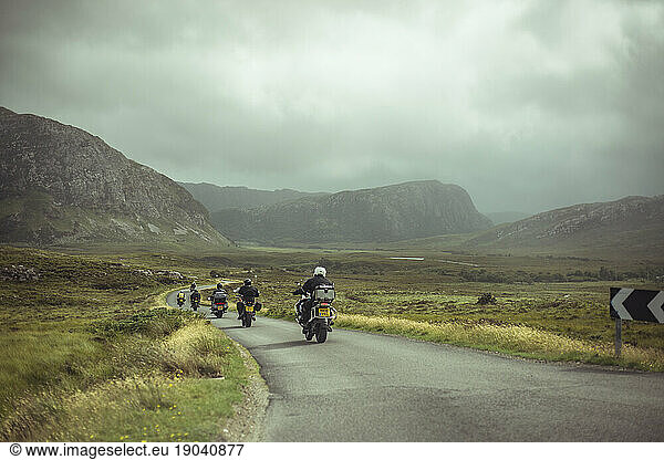 Line of motorbikes ride on small winding road through remote mountians