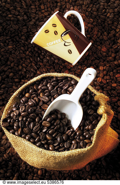 Linen sack filled with coffee beans with wooden scoop atop a bed of coffee beans
